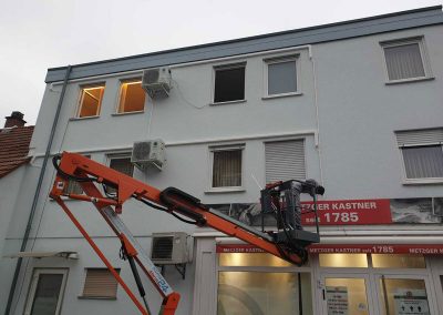 ein Mann auf einer Hubarbeitsbühne vor einem Gebäude und installiert Klimaanlagen