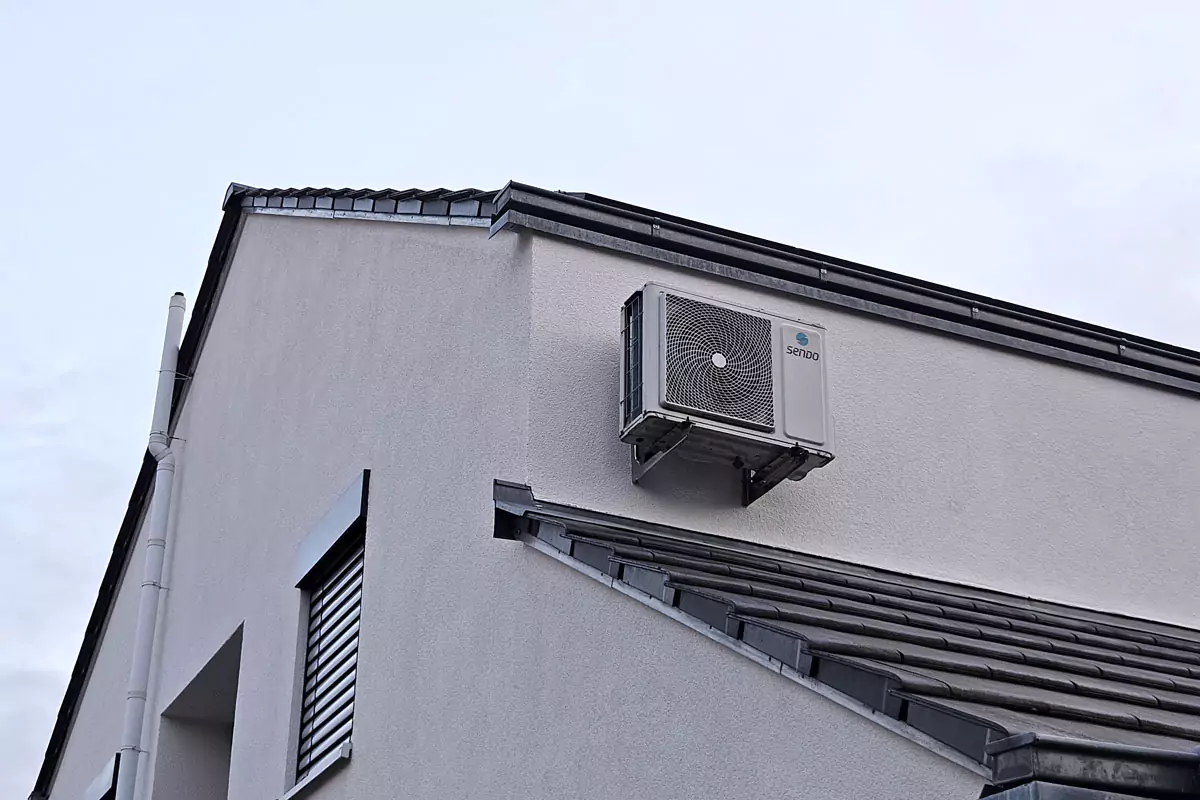 Eine Klimaanlage, die an der Außenwand eines Gebäudes mit geneigtem Dach installiert ist.