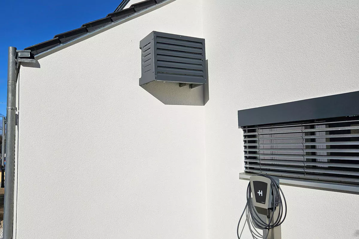 An der Wand montierte Außenklimaanlage mit einem Ladegerät für Elektrofahrzeuge daneben.