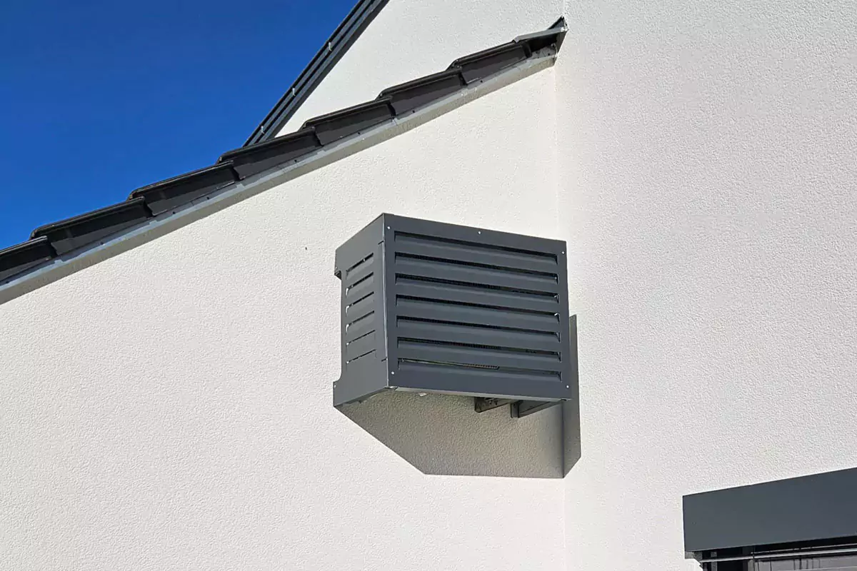 Außenwandlüftung an einem weißen Gebäude unter strahlend blauem Himmel.